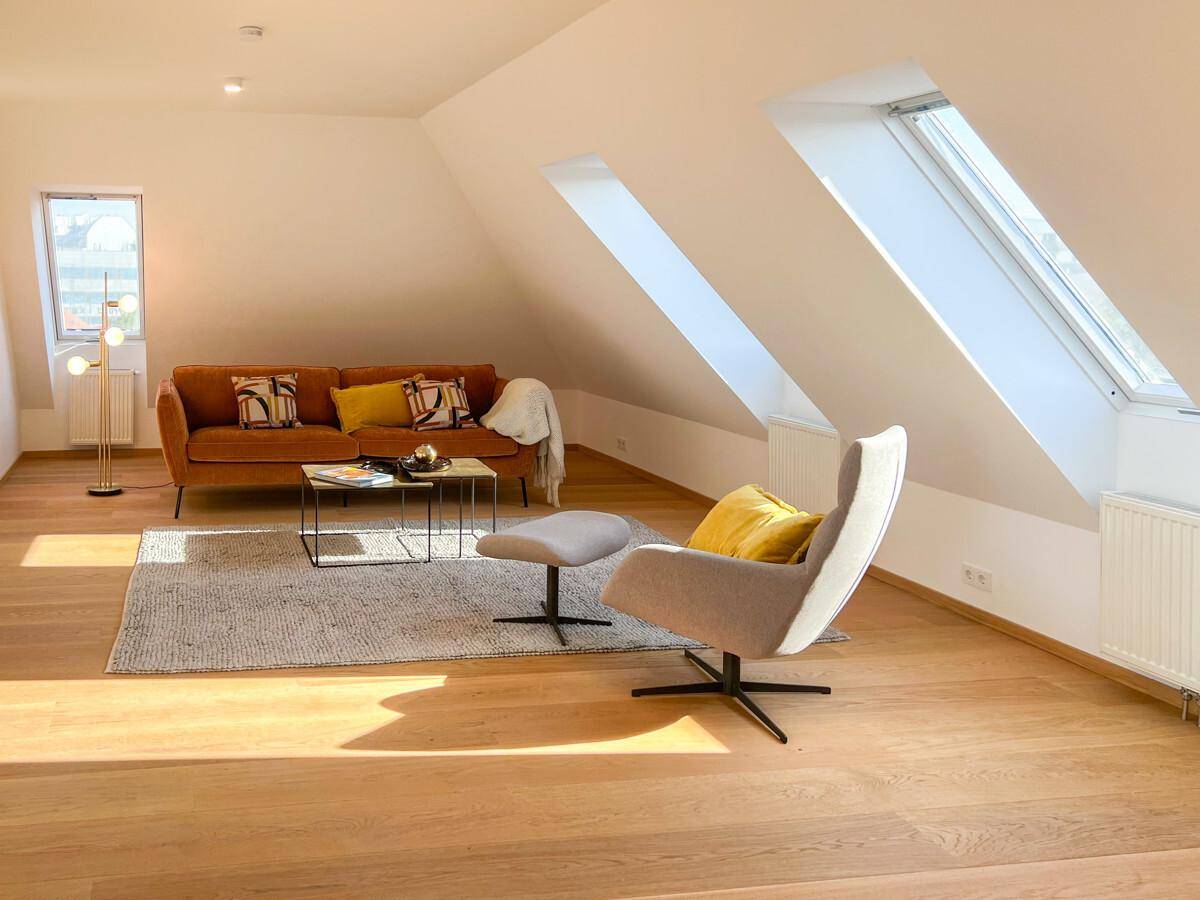 Geräumiges und helles Wohnzimmer im Dachgeschoss mit bequemer Couch und Holzboden.