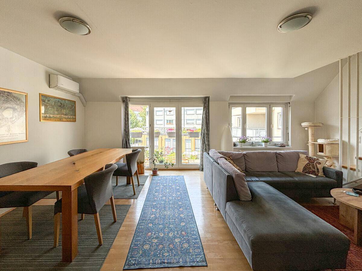 Heller Wohn- und Essbereich mit Holztisch, großem Sofa und Zugang zum Balkon.