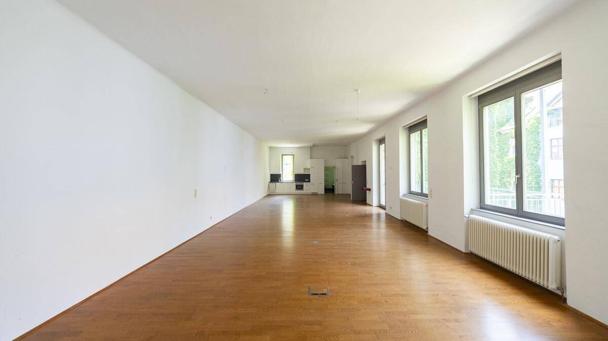 Langer, heller Wohnbereich mit Holzboden und Blick auf die offene Küchenzeile im Hintergrund.