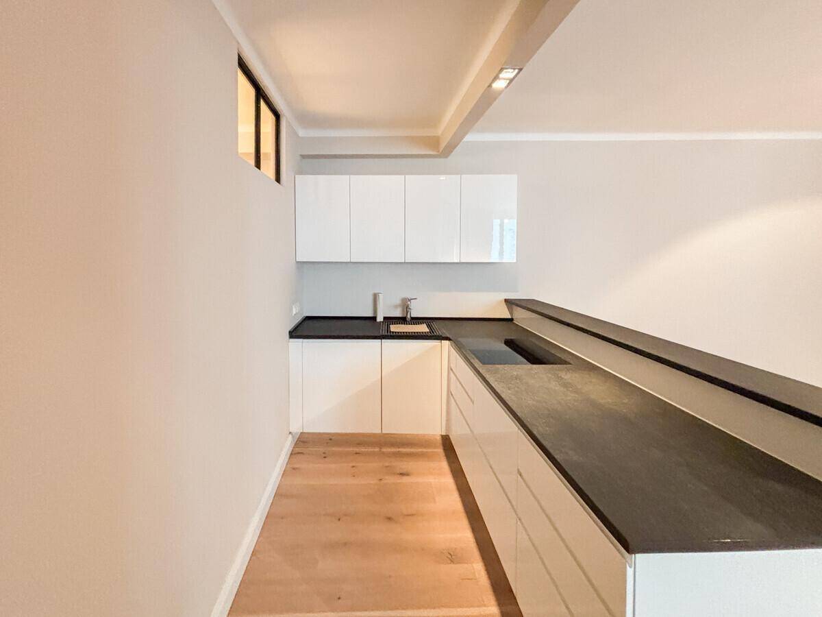 Moderne Küchenzeile mit weißen Hochglanzschränken, dunkler Arbeitsplatte und integriertem Spülbecken.