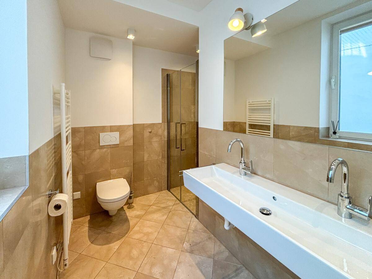 Modernes Badezimmer mit Doppelwaschbecken, begehbarer Dusche und beigen Wand- und Bodenfliesen.