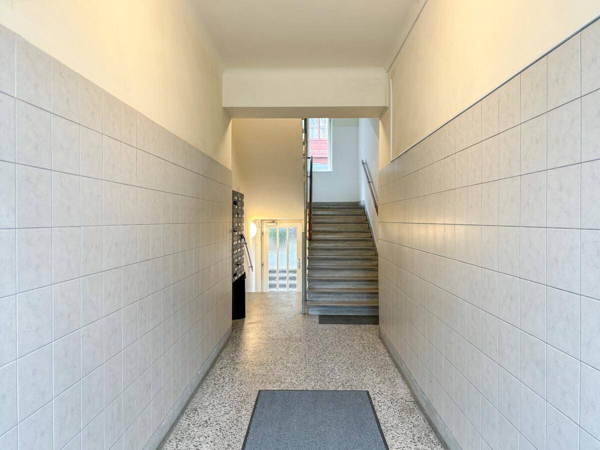 Eingangsbereich mit gefliesten Wänden, Terrazzoboden und Treppenaufgang zu den oberen Etagen.