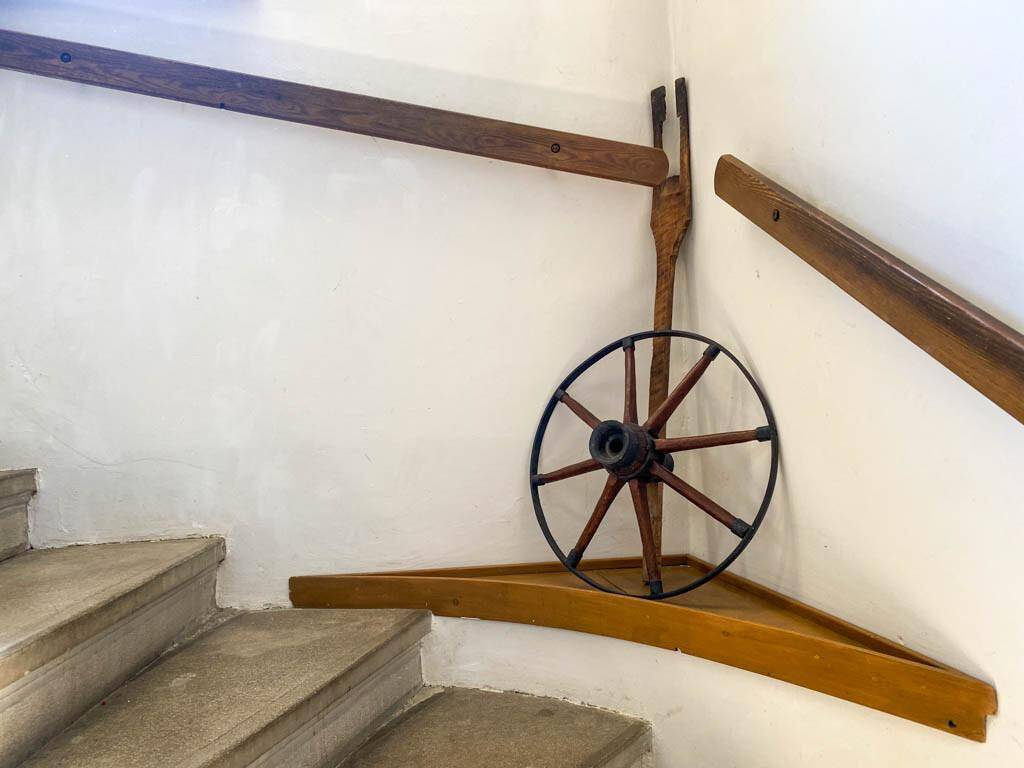 Detailansicht einer Steintreppe mit Holzgeländer und einem dekorativen Wagenrad.