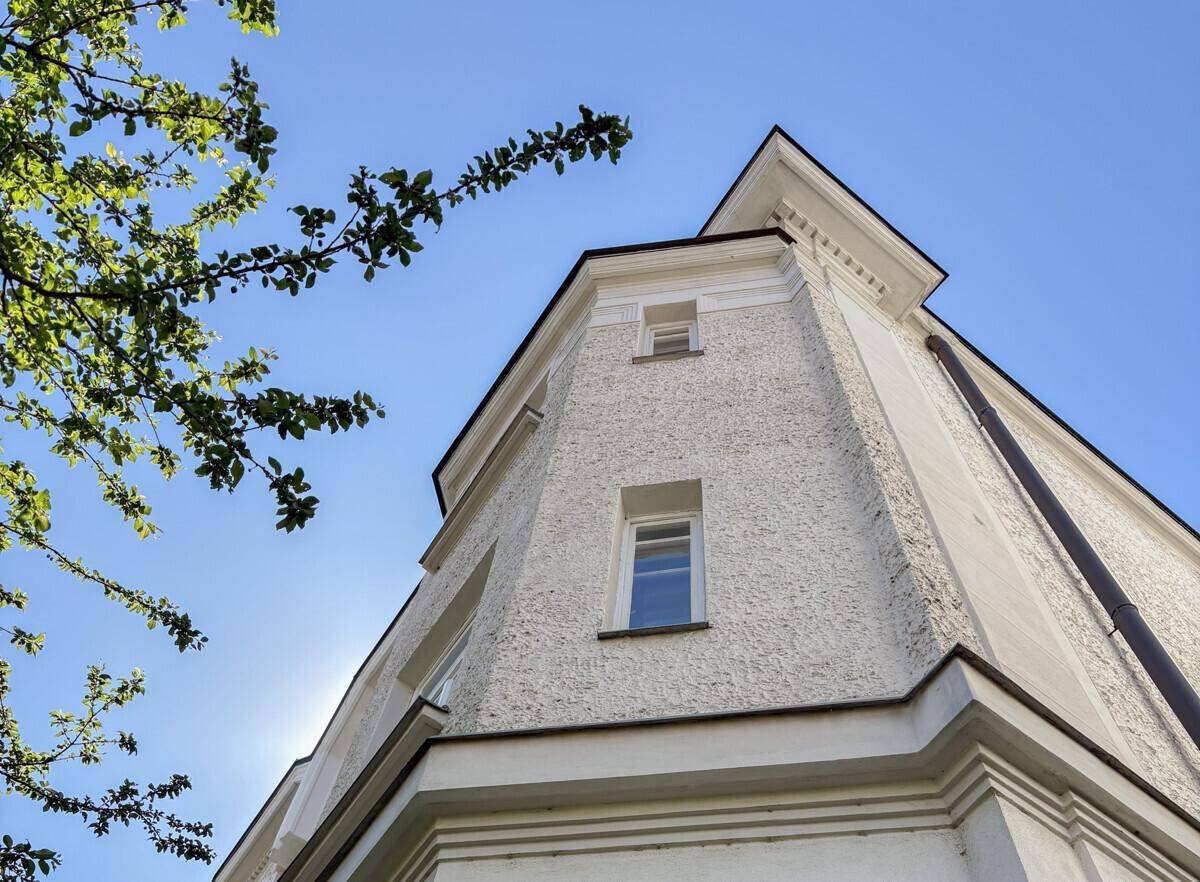 Blick auf die helle Fassade eines Eckgebäudes mit kleinen Fenstern unter blauem Himmel.
