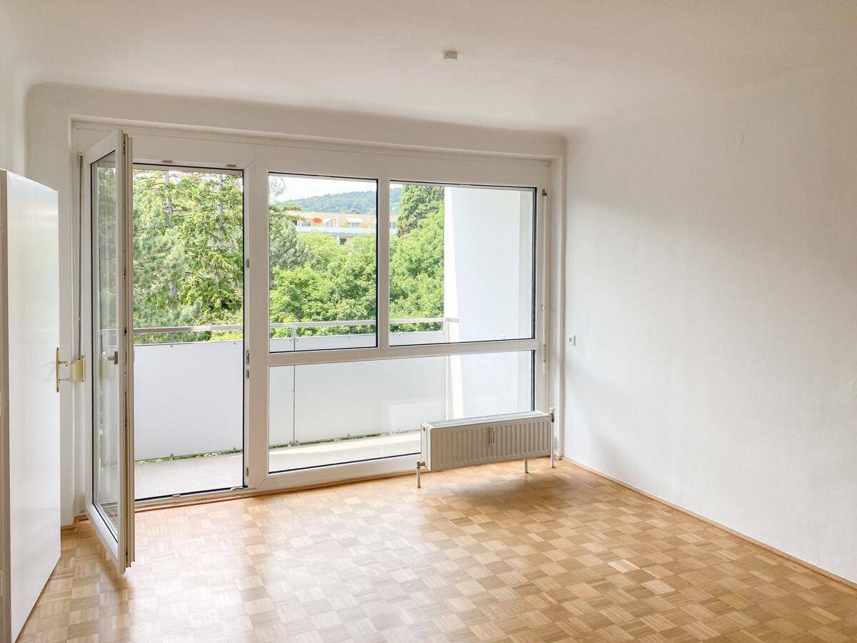 Geräumiges Zimmer mit Parkettboden, großen Fenstern und direktem Zugang zum Balkon.