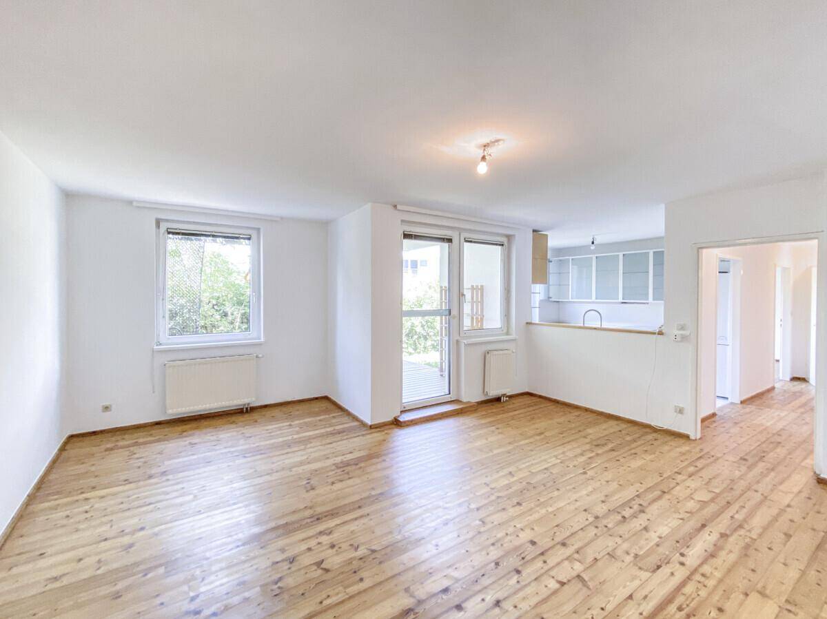 Helles Wohnzimmer mit Holzboden und Zugang zur Terrasse, offen zum Küchenbereich.