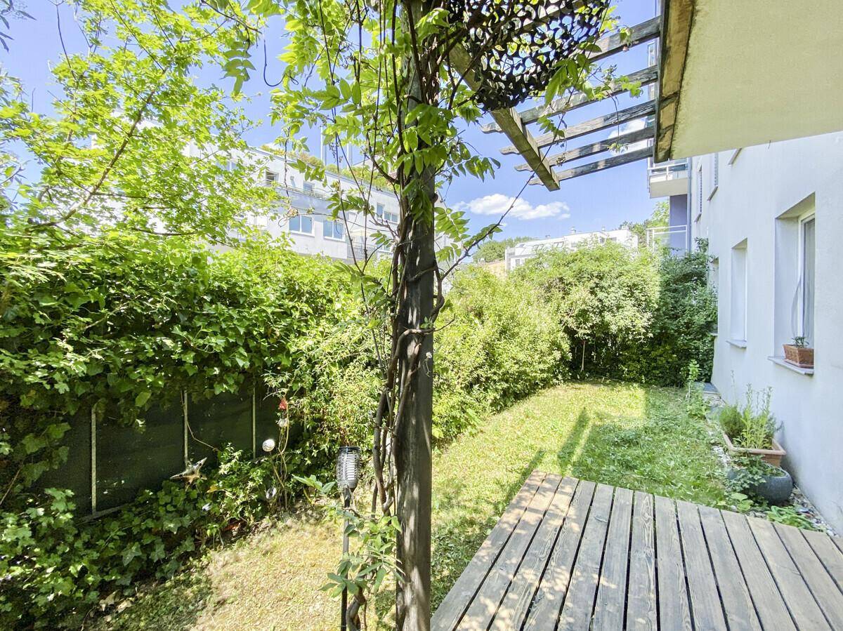Blick auf den gepflegten Garten mit Holzterrasse und grüner Hecke unter blauem Himmel.