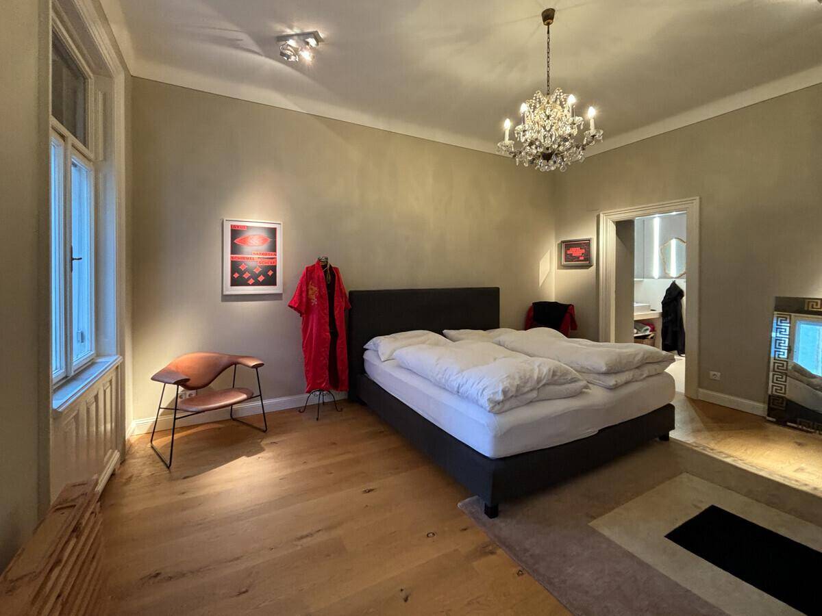 Gemütliches Schlafzimmer mit Doppelbett, Holzboden und elegantem Kronleuchter.