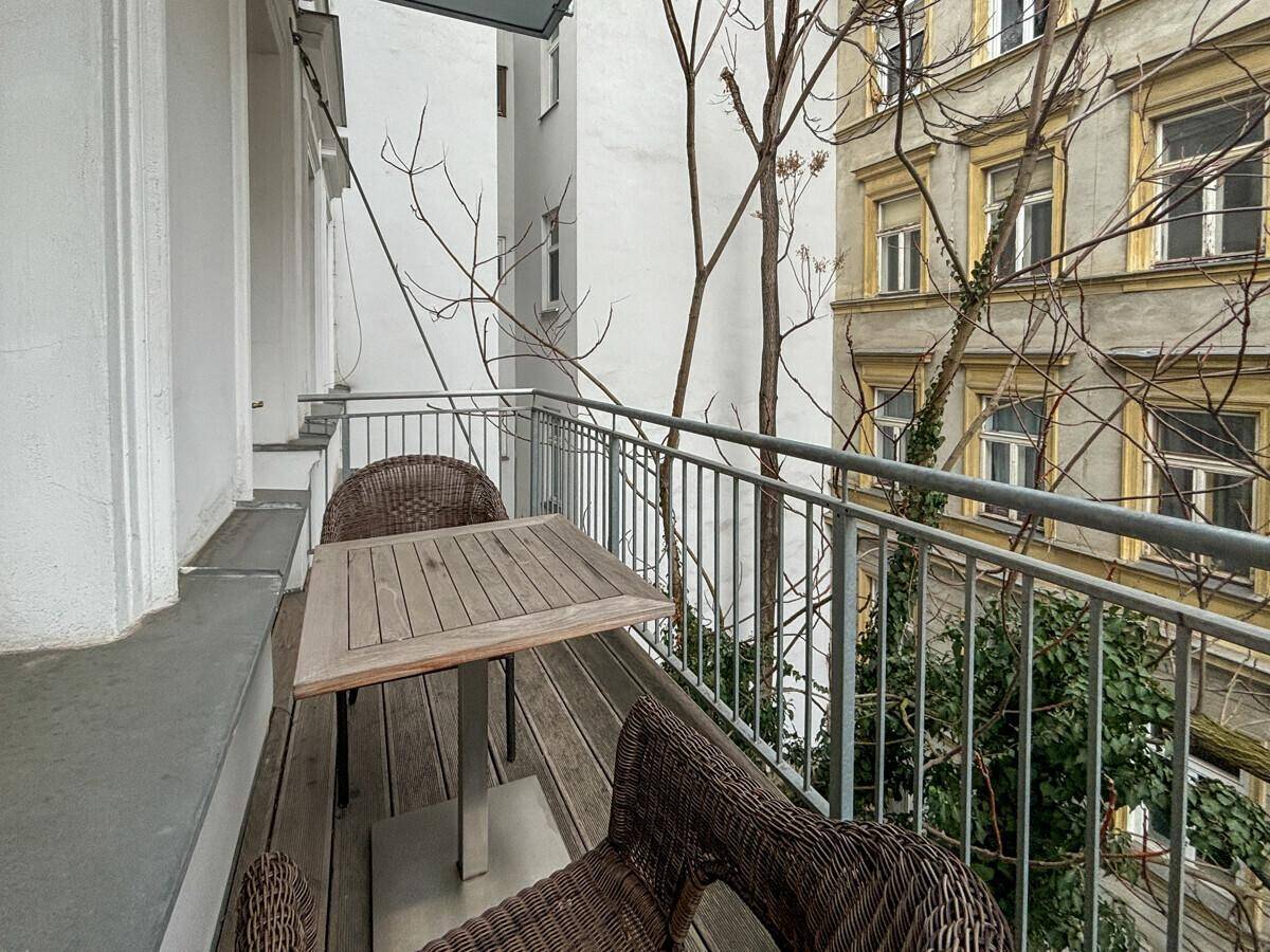 Gemütlicher Balkon mit Holzboden und Sitzgelegenheiten, umgeben von Bäumen.