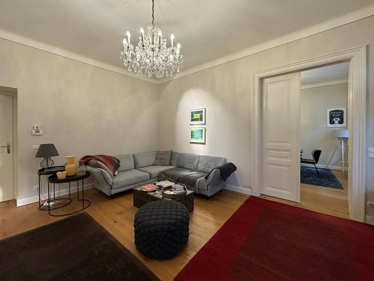 Helles Wohnzimmer mit bequemer Couch, Holzboden und elegantem Kronleuchter.
