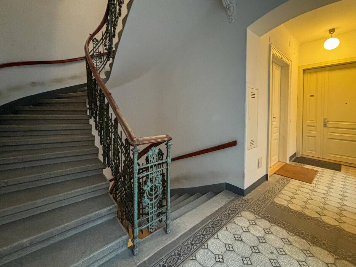 Historisches Treppenhaus mit kunstvollem Geländer und gemusterten Fliesen im Eingangsbereich.