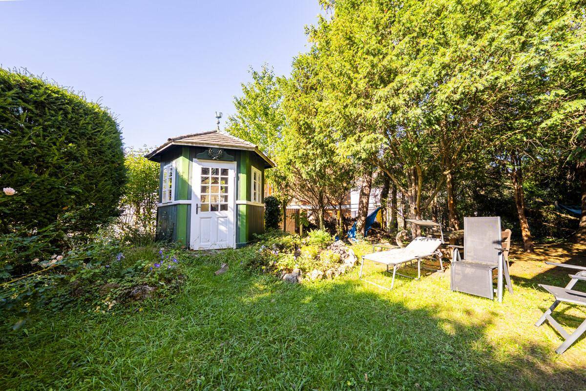 Idyllischer Garten mit einem charmanten grünen Pavillon und Liegestühlen unter schattenspendenden Bäumen.