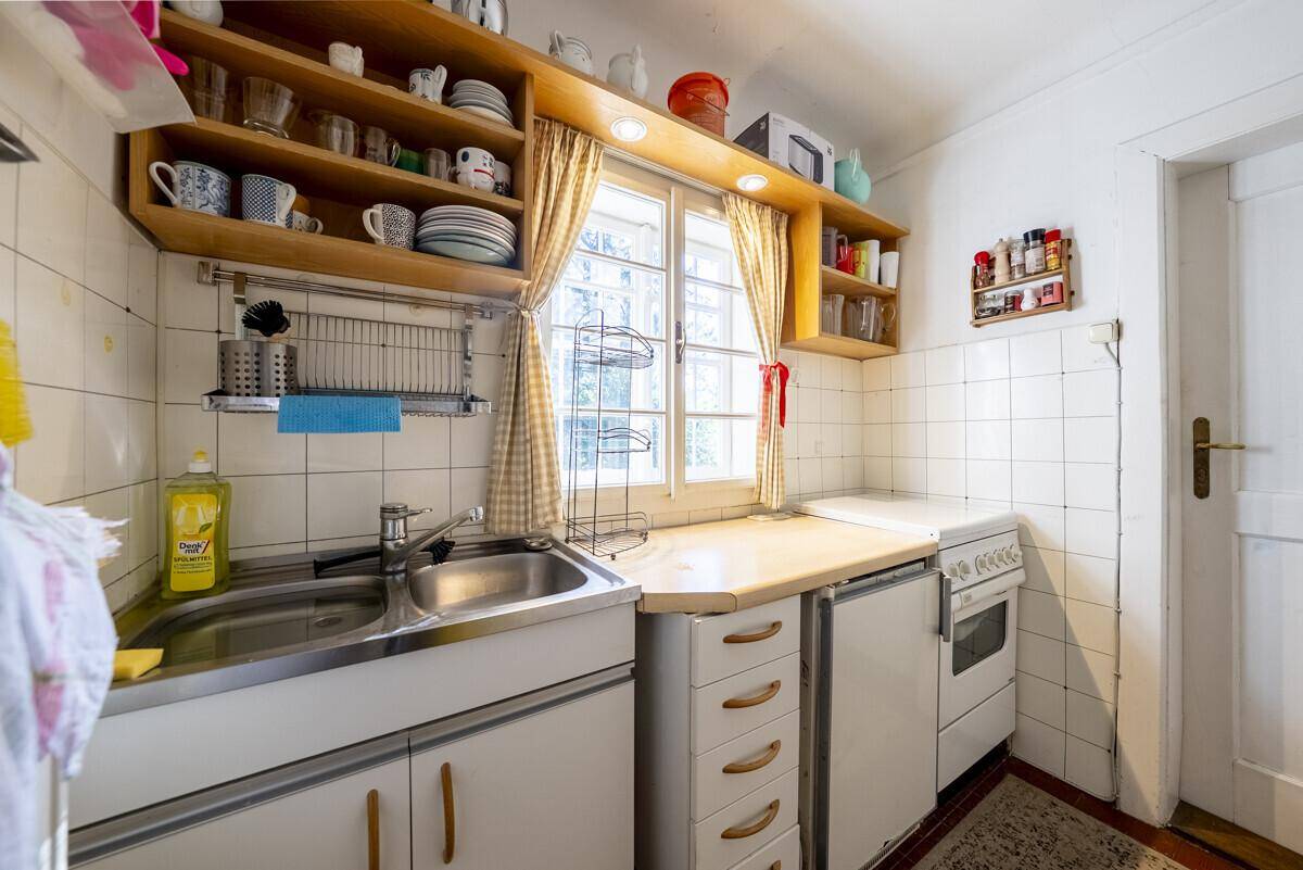 Kleine, funktionale Küche mit weißen Unterschränken, Spüle und einem Fenster für natürliches Licht.