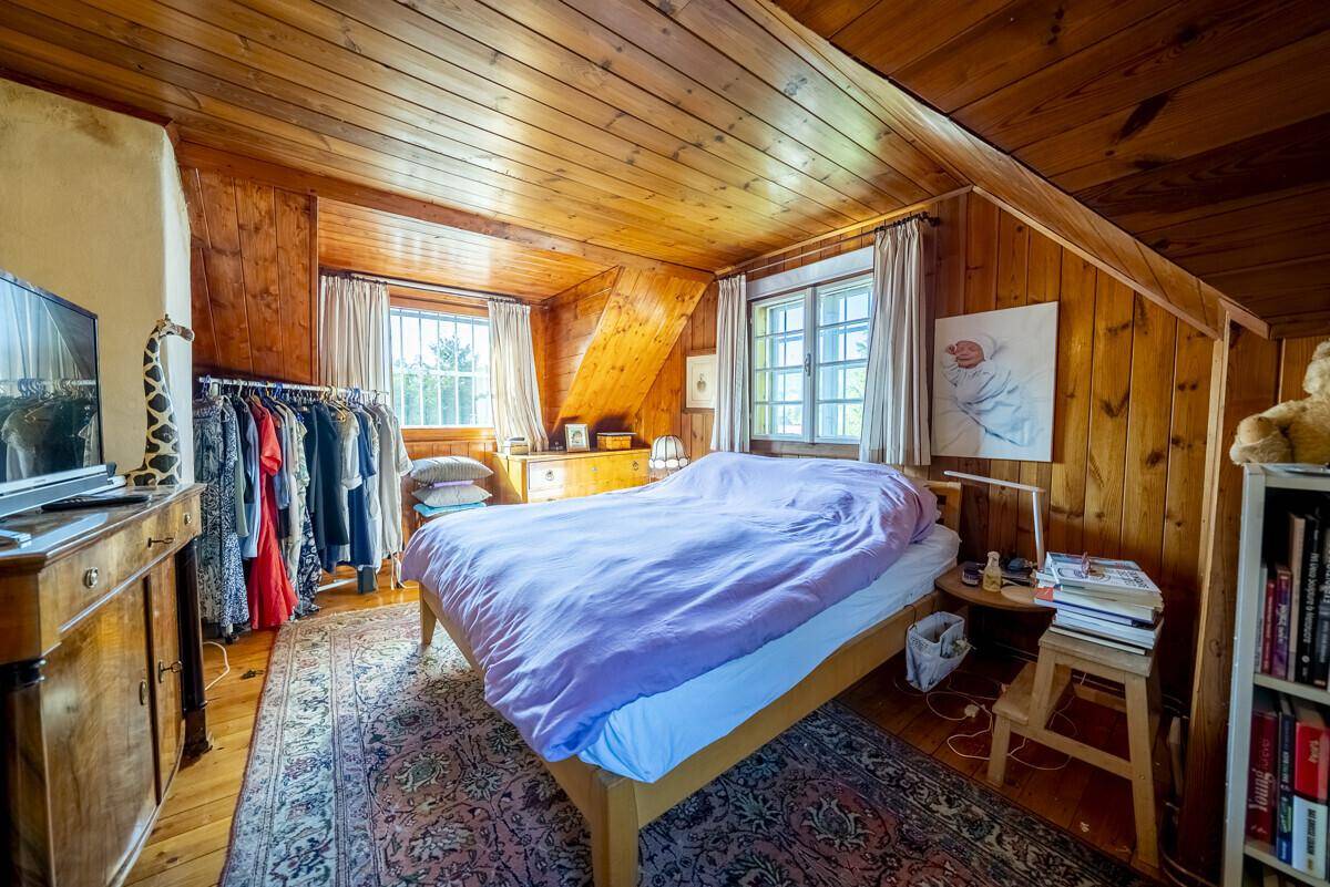 Rustikales Schlafzimmer mit Holzboden und Dachschrägen, ausgestattet mit einem Doppelbett und Kleiderstange.