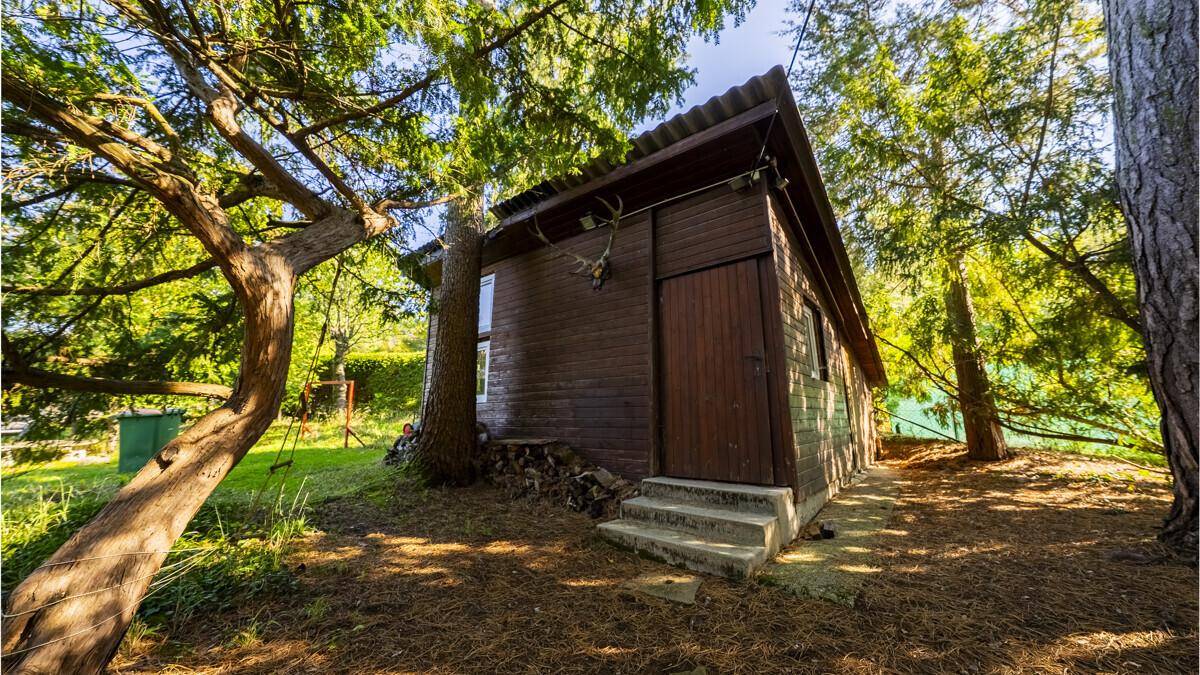 Rustikale Holzhütte im Grünen, umgeben von Bäumen, mit einfacher Holzfassade und Treppenzugang.