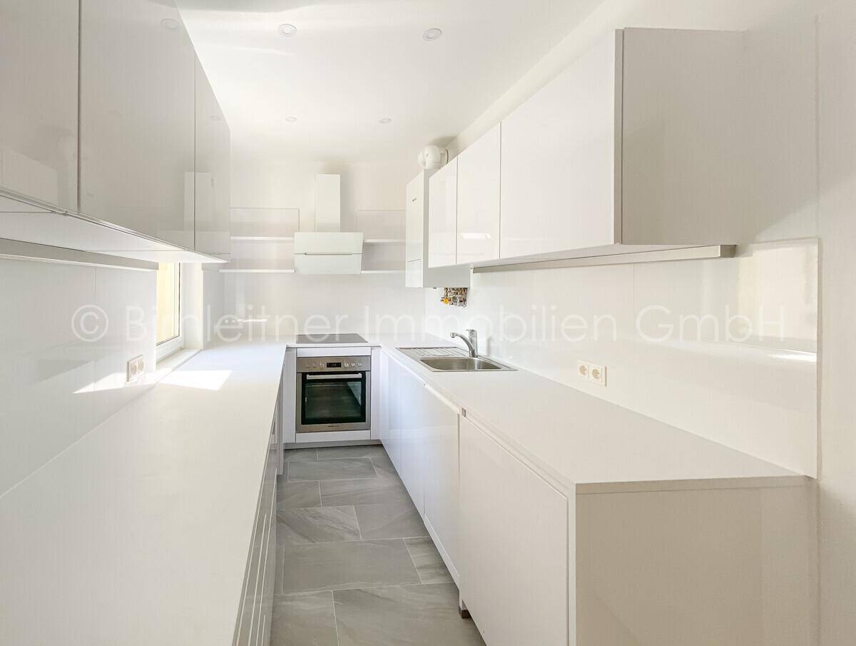 Moderne, schmale Küche mit weißen Hochglanzschränken, integriertem Backofen und Fliesenboden.