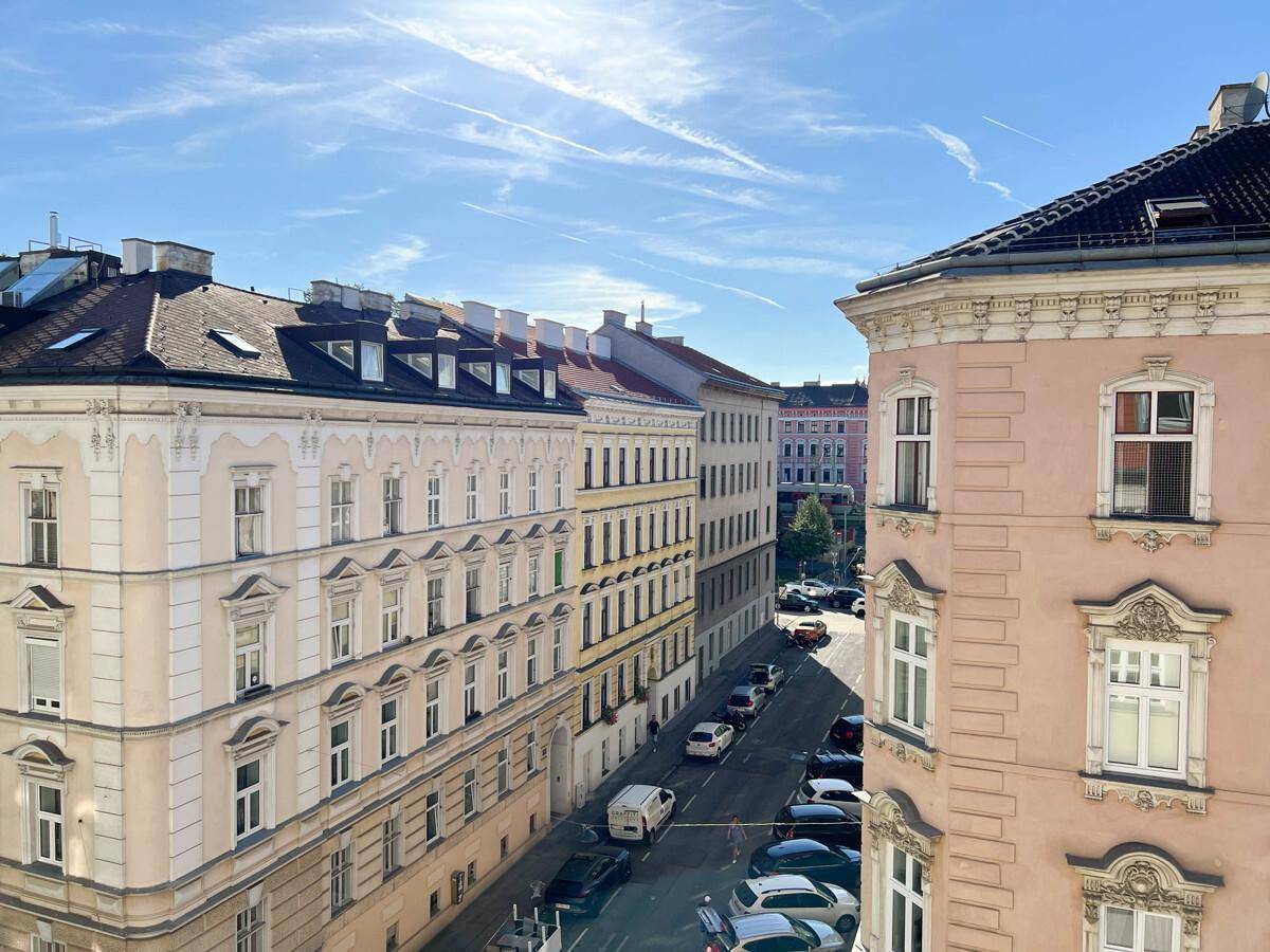 Blick auf eine belebte Stadtstraße mit historischen Gebäuden und parkenden Autos.