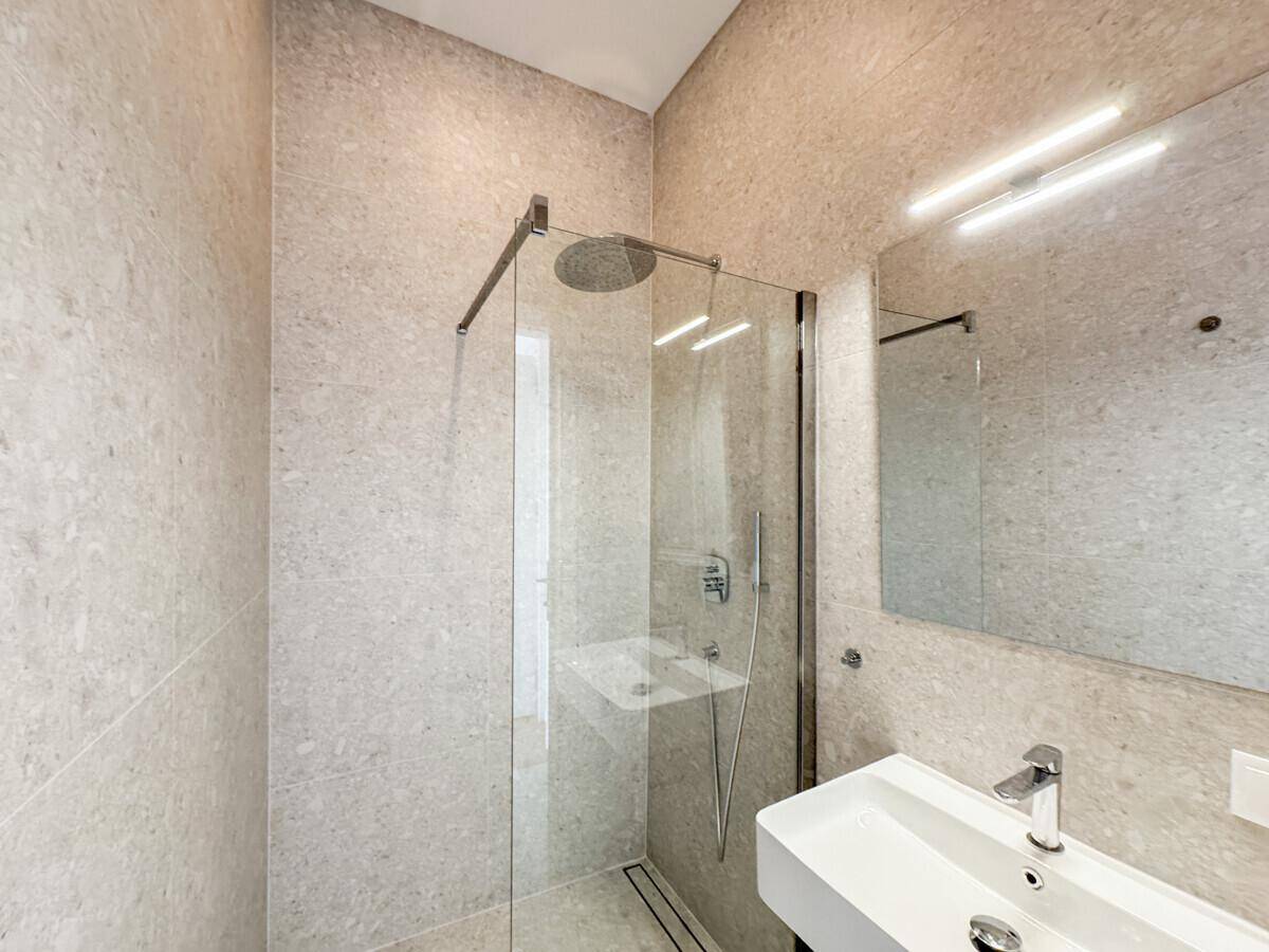 Modernes Badezimmer mit begehbarer Dusche, hellgrauen Fliesen und einem einzelnen Waschbecken.