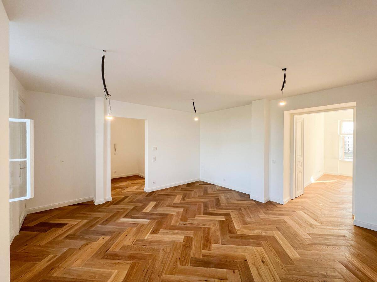 Geräumiges Zimmer mit Fischgrätparkett, viel Tageslicht und offenen Türen zu angrenzenden Räumen.