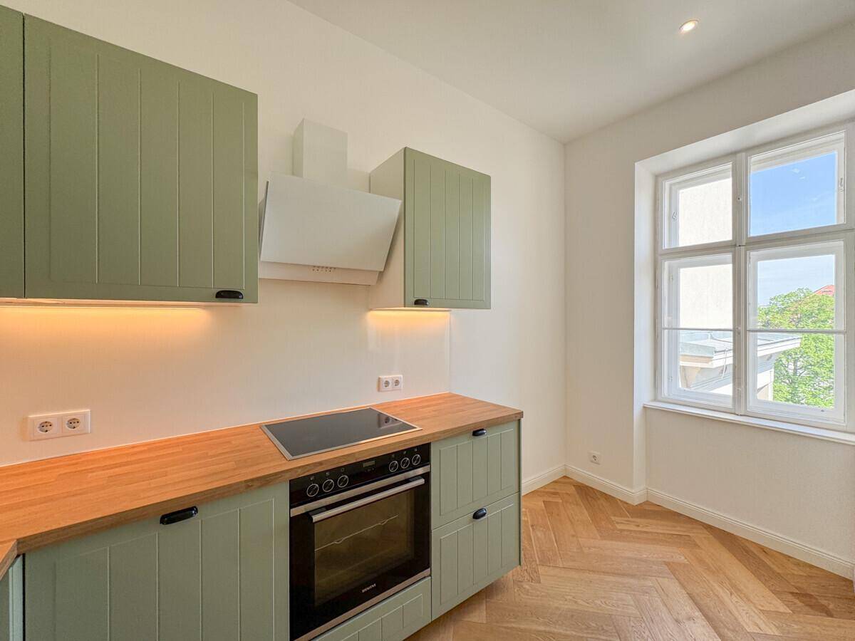 Detailansicht der modernen Küche mit hellgrünen Schränken, Backofen und Fenster.