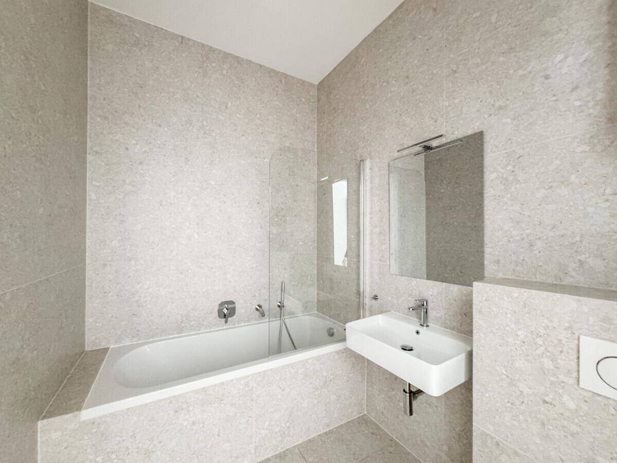 Modernes Badezimmer mit hellgrauen Fliesen, Badewanne und einem einzelnen Waschbecken.