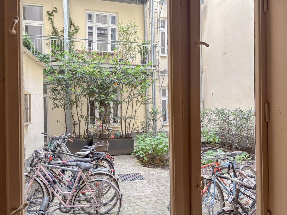 Grüner Innenhof mit Fahrradabstellplätzen und Pflanzen, gesehen durch ein Fenster.