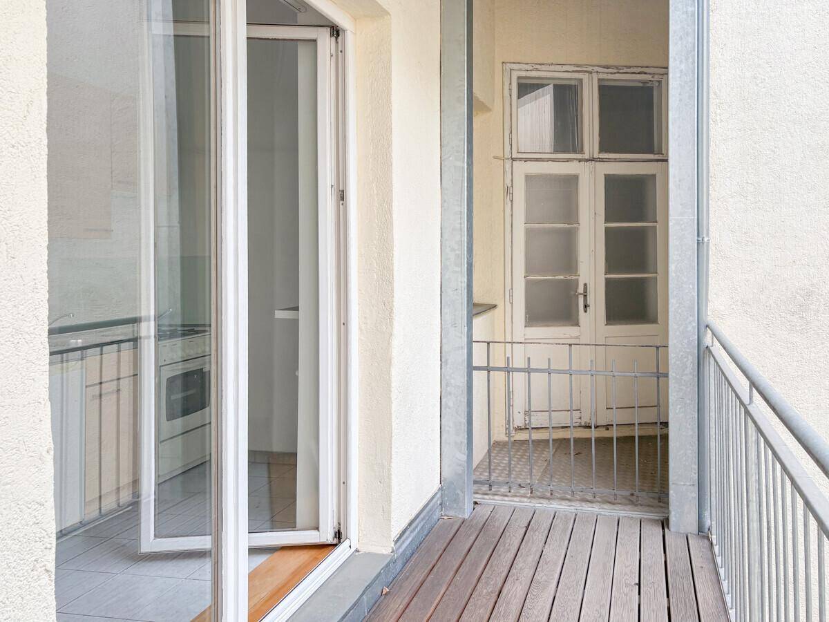 Kleiner Balkon mit Holzboden und Blick auf einen weiteren Balkon und eine Küche.