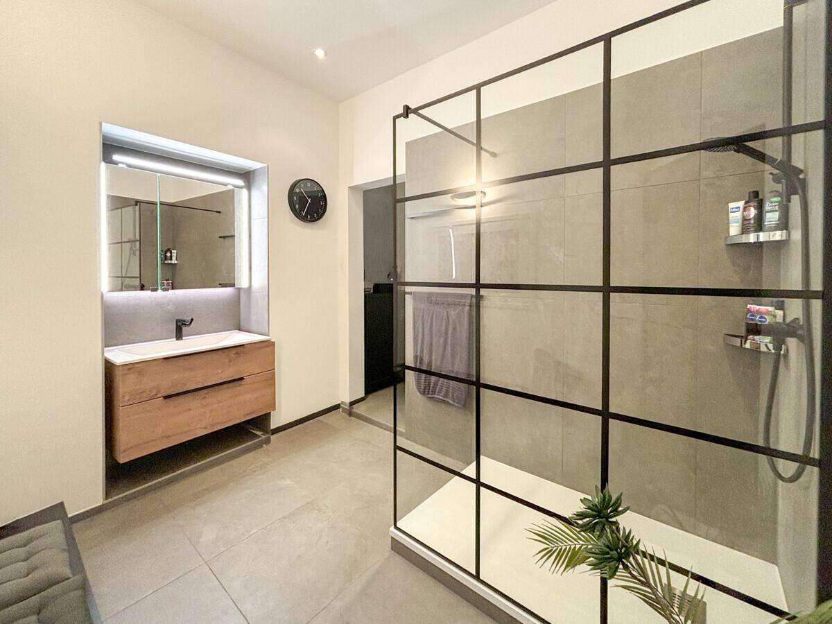 Modernes Badezimmer mit großer begehbarer Dusche, elegantem Waschtisch und grauen Fliesen.