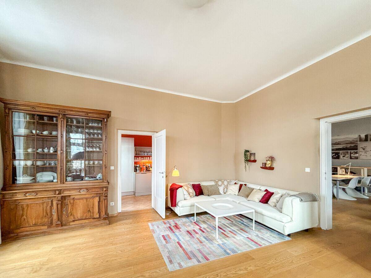 Gemütliches Wohnzimmer mit großem Ecksofa, antiker Holzvitrine und Zugang zu einer modernen Küche.