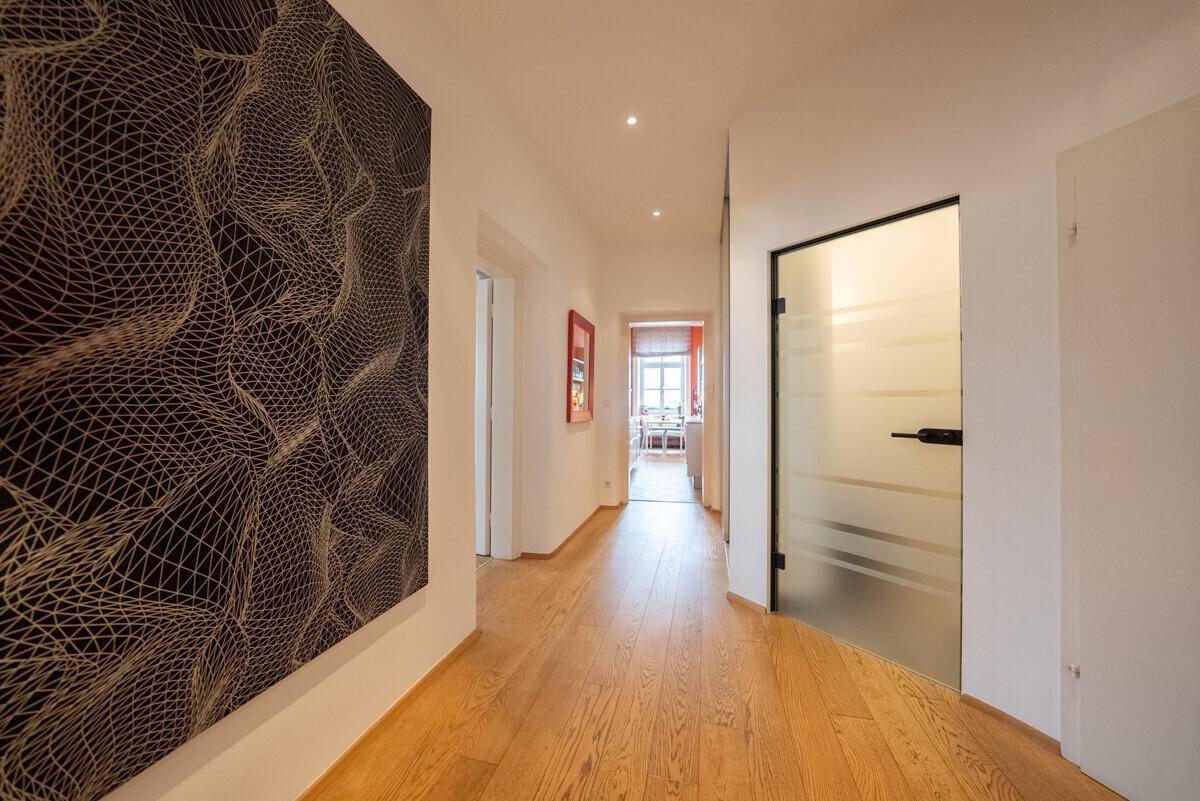Heller Flur mit Holzboden, moderner Kunst und einer eleganten Milchglastür, die zu weiteren Räumen führt.