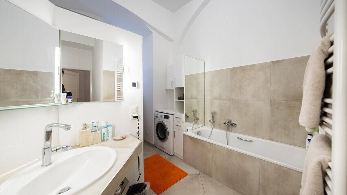 Helles Badezimmer mit Badewanne, Waschmaschine und einem beheizten Handtuchhalter.