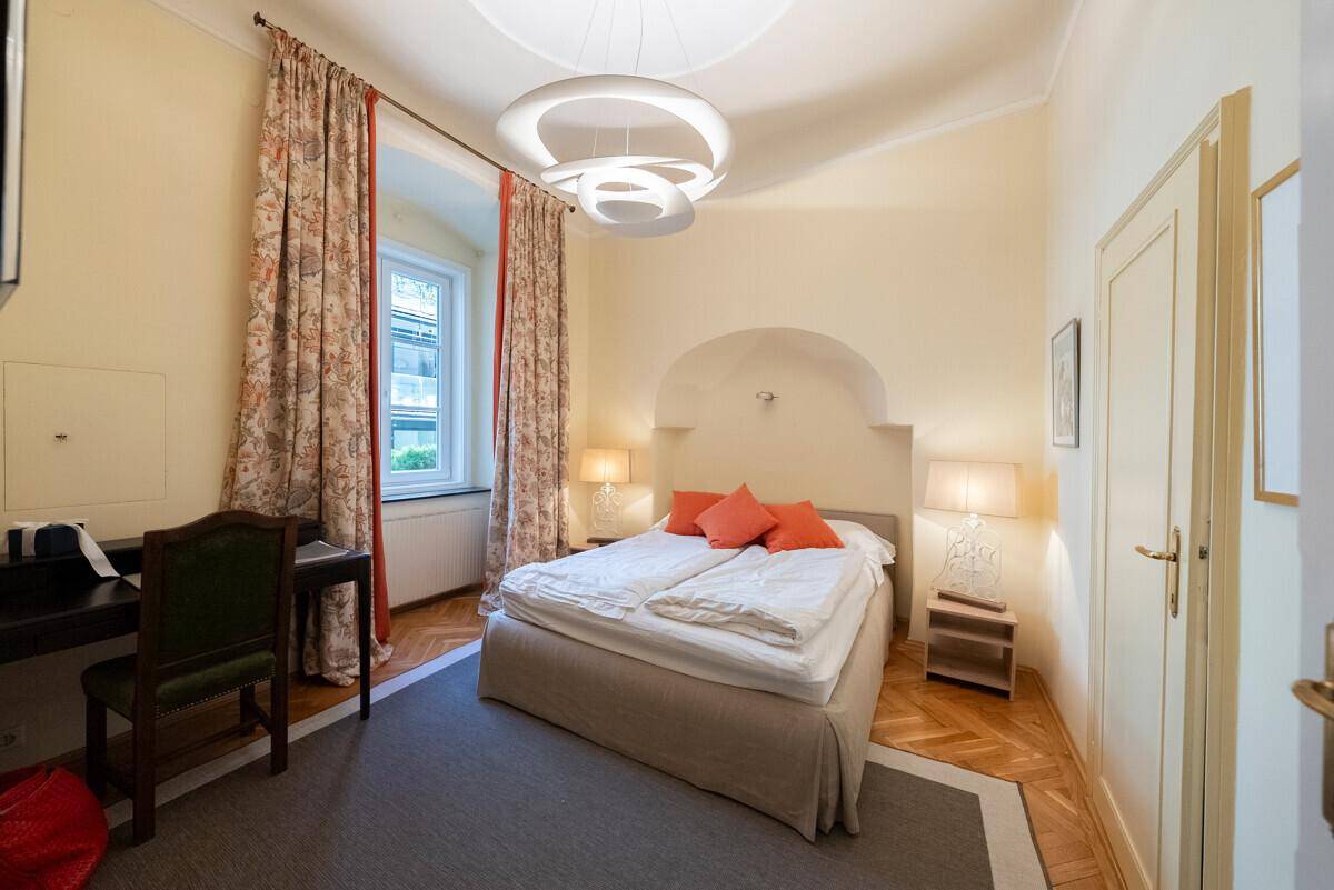 Gemütliches Schlafzimmer mit Parkettboden, Doppelbett und floralen Vorhängen am Fenster.