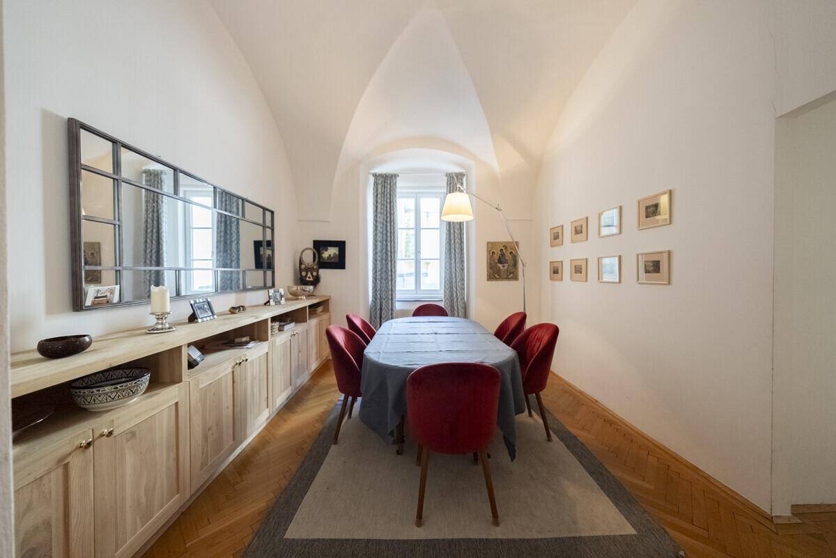 Elegantes Esszimmer mit Gewölbedecke, Holzboden und einem langen Esstisch mit roten Stühlen.