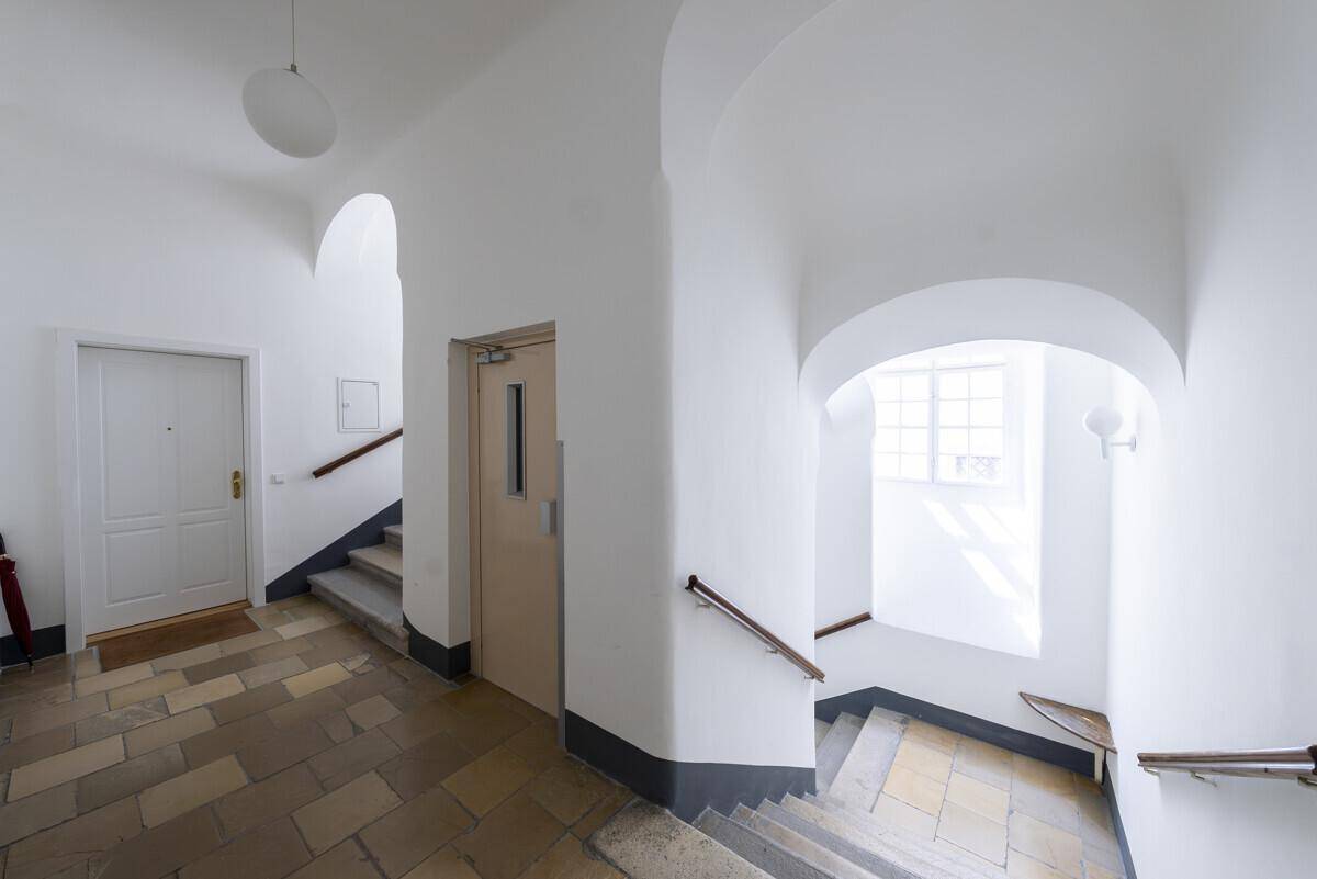 Heller Treppenaufgang mit Steinboden, Geländer und einem Aufzug im historischen Gebäude.