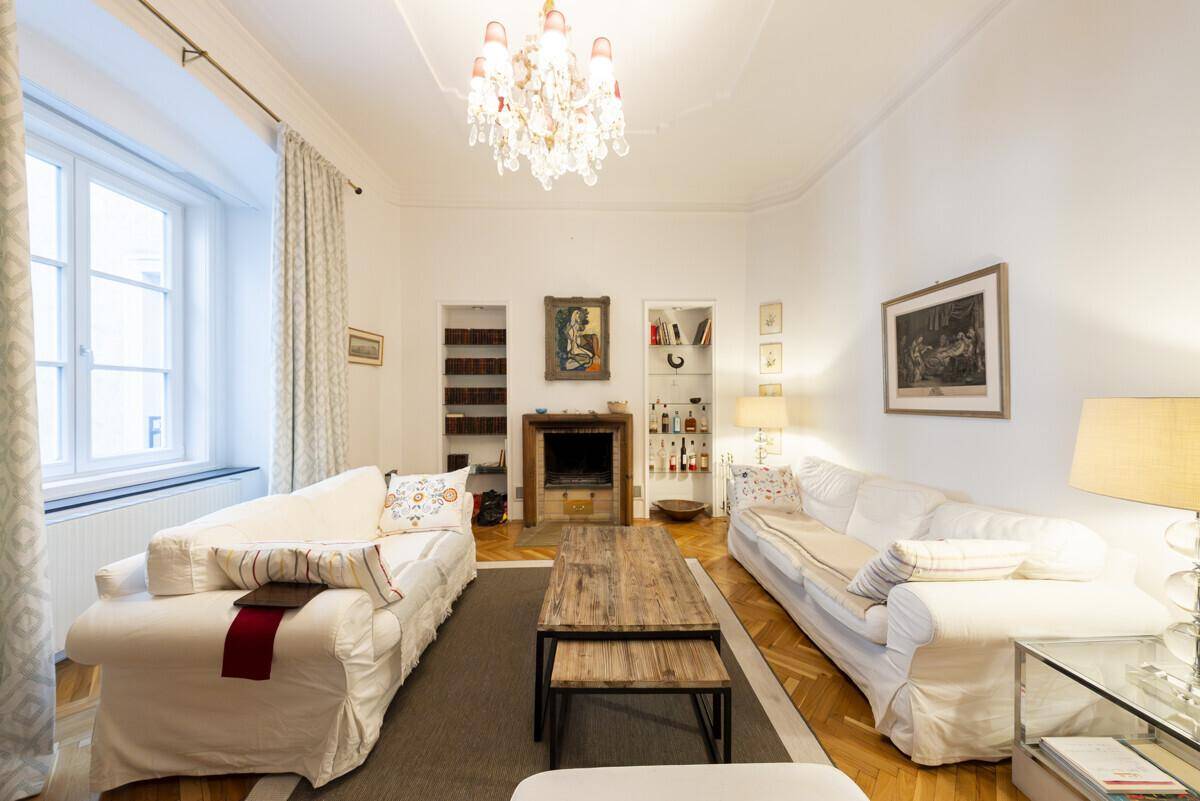 Helles Wohnzimmer mit Parkettboden, Kamin und einem opulenten Kronleuchter an der Decke.