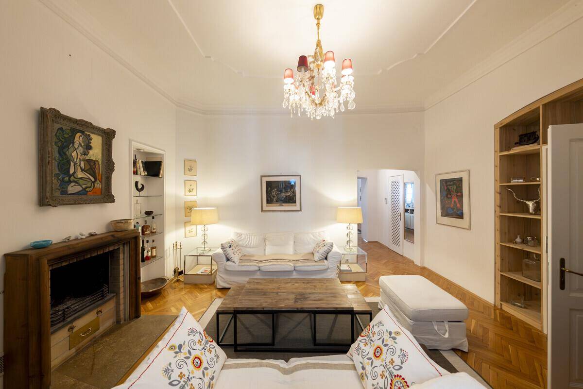 Geräumiges Wohnzimmer mit klassischem Kamin, Parkettboden und einem dekorativen Kronleuchter.