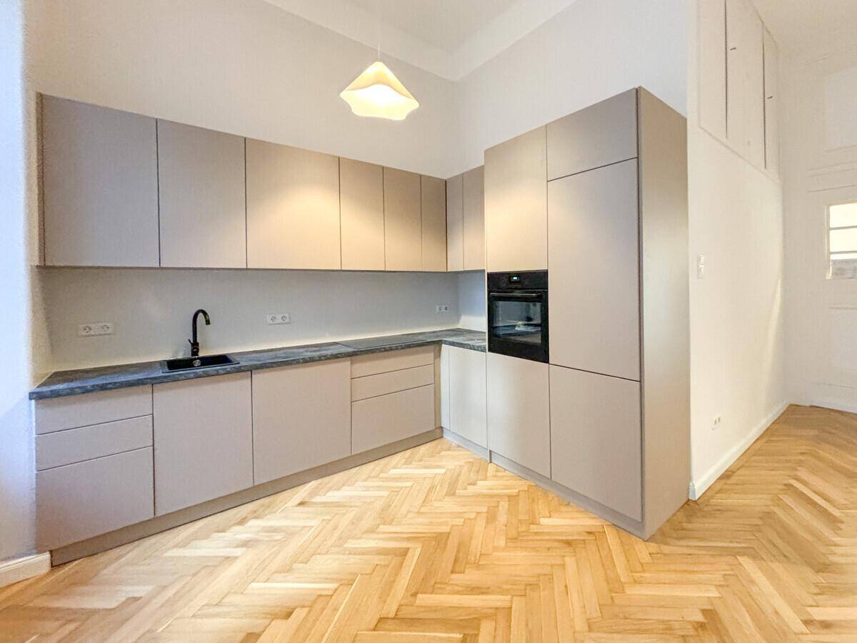 Neue, moderne Küche mit hellgrauen Fronten, integriertem Backofen und dunkler Arbeitsplatte.