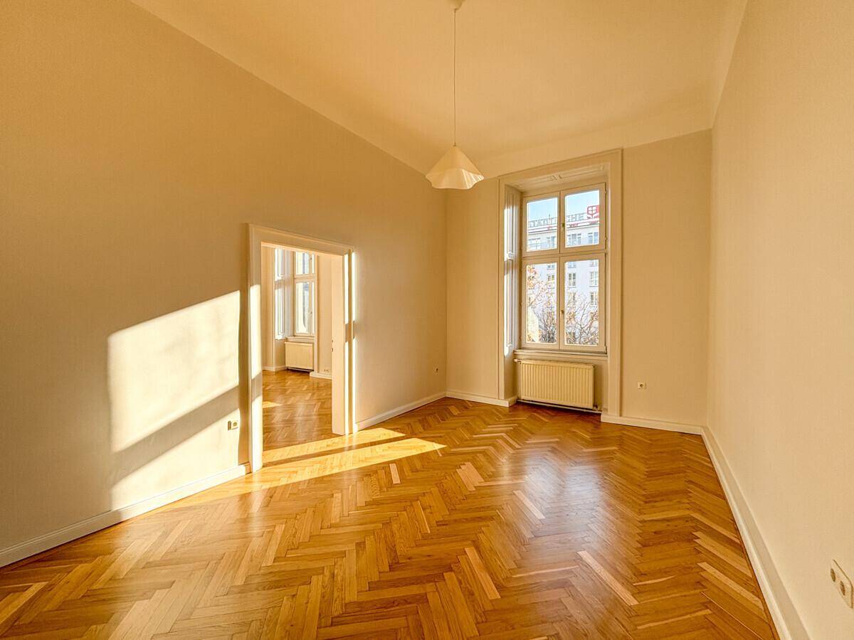 Geräumiges Zimmer mit Fischgrätparkett, hohen Decken und einem großen Fenster, das viel Licht spendet.