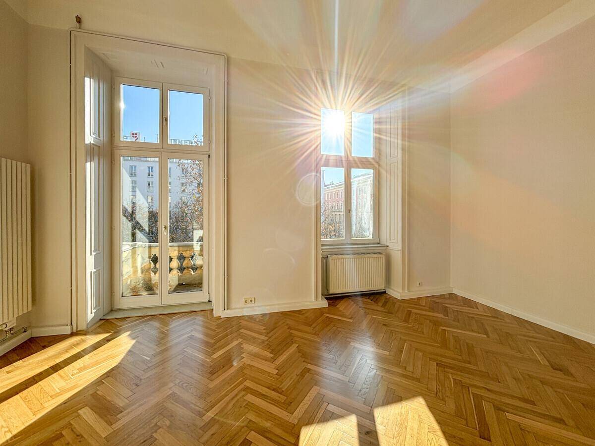 Geräumiges Zimmer mit klassischem Fischgrätparkett und großen Fenstern, die den Raum mit Sonnenlicht füllen.