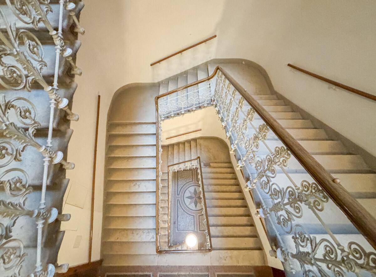 Elegantes Treppenhaus in einem Altbau mit kunstvollen Geländern und Holzhandläufen.