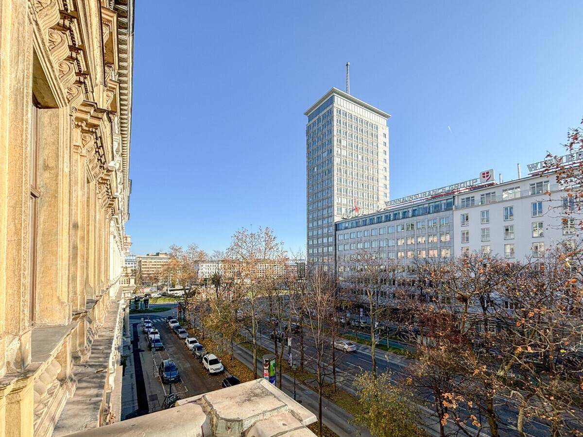 Balkonblick auf eine belebte Stadtstraße mit modernen und klassischen Gebäuden unter blauem Himmel.