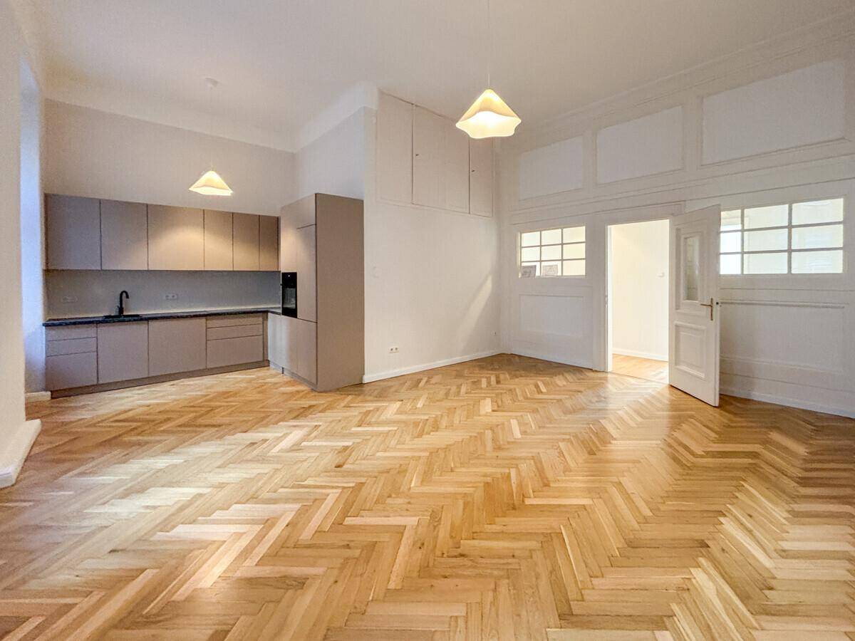 Offener Wohnbereich mit integrierter moderner Küche und Fischgrätparkett, ideal für geselliges Beisammensein.