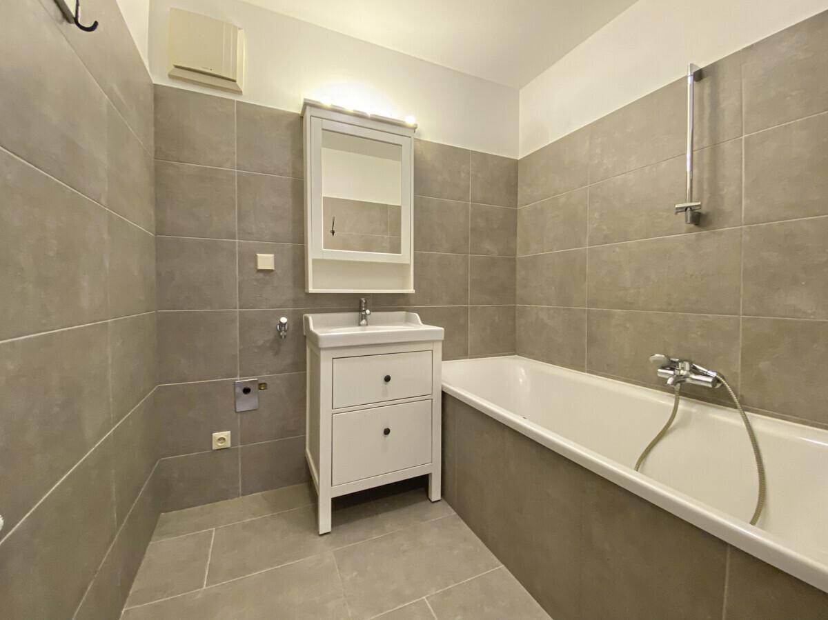 Modern gefliestes Badezimmer in Grau mit Badewanne, Einzelwaschbecken und Spiegelschrank.