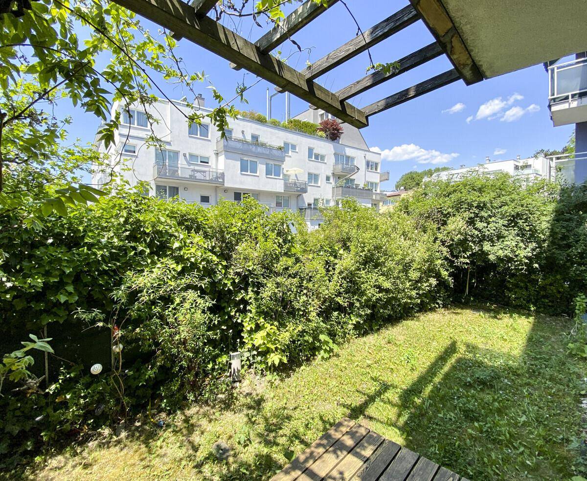 Gepflegter Garten mit üppiger Vegetation und sonnigem Rasen, umgeben von Wohnbebauung.
