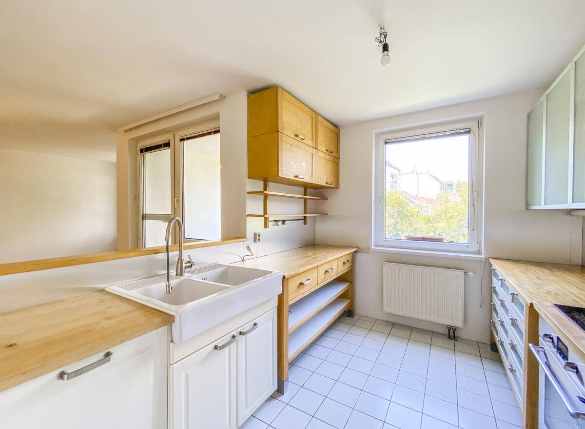 Funktionale Küche mit weißen Unterschränken, Holz-Arbeitsplatten und Fenster zum Garten.