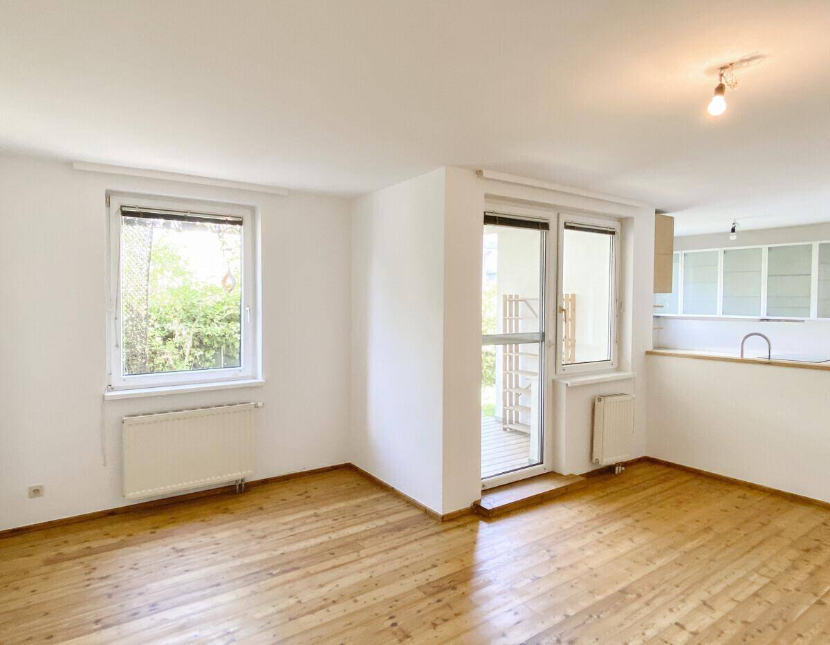 Geräumiges Wohnzimmer mit Parkettboden und großen Fenstern, die viel Tageslicht hereinlassen.