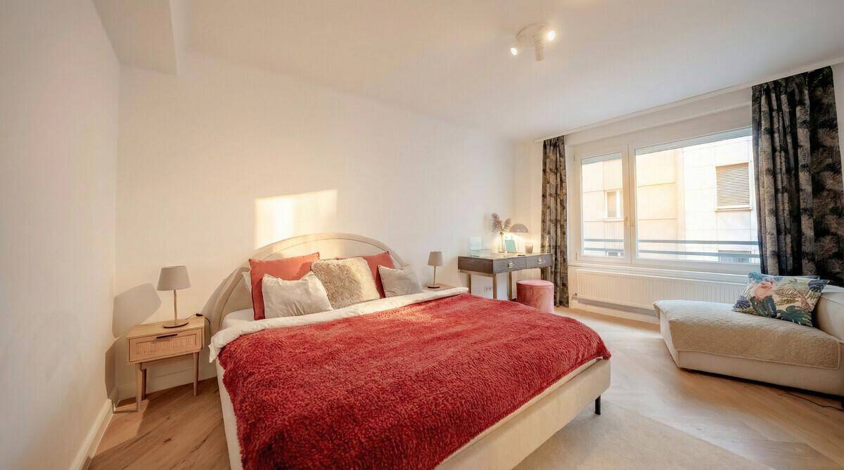 Gemütliches Schlafzimmer mit rotem Bett, Parkettboden und großem Fenster, hell und komfortabel.