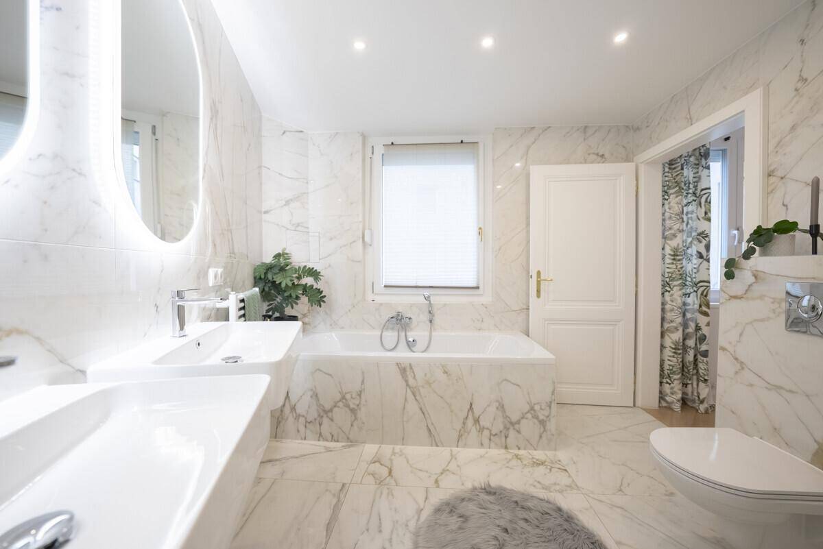 Elegantes Badezimmer mit Marmorverkleidung, Badewanne, Doppelwaschbecken und WC, hochwertig ausgestattet.