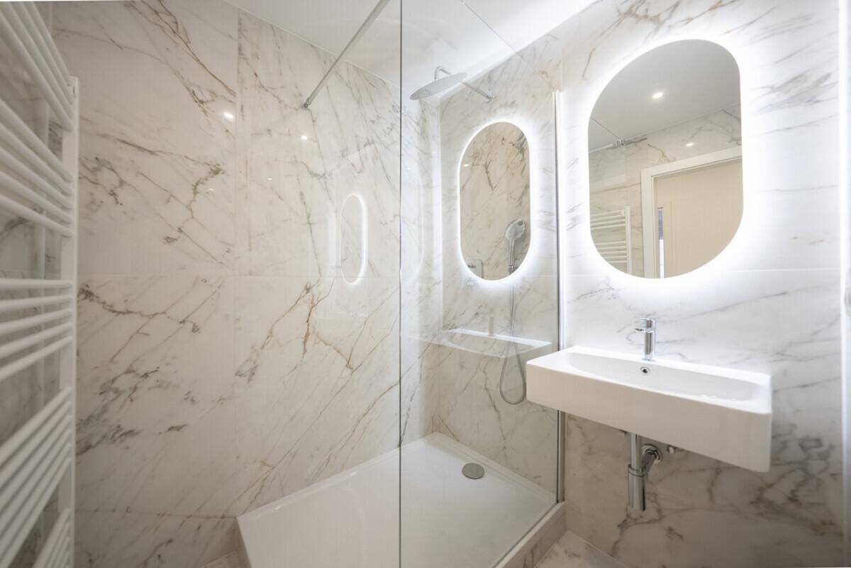 Modernes Badezimmer mit Marmorfliesen, begehbarer Dusche und beleuchtetem Spiegel, sehr stilvoll.