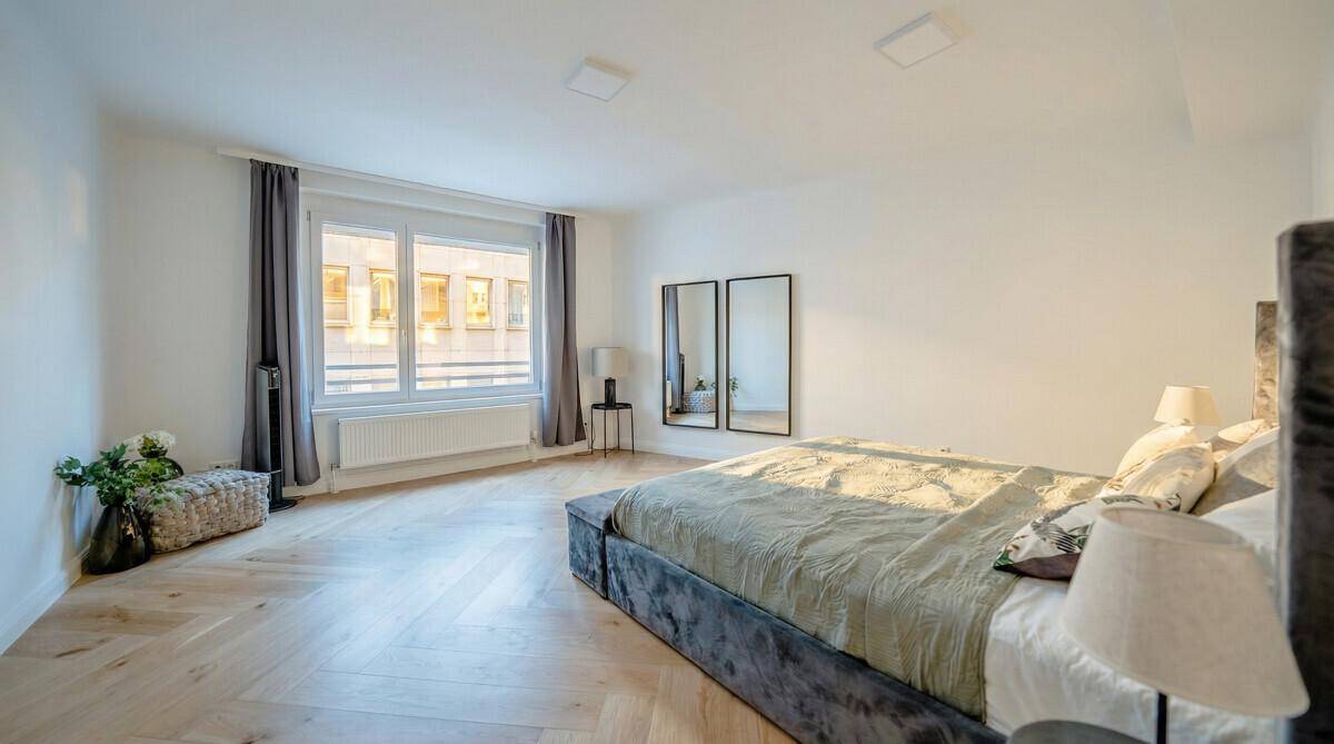 Geräumiges Schlafzimmer mit Parkettboden, großem Bett und viel natürlichem Licht, modern eingerichtet.
